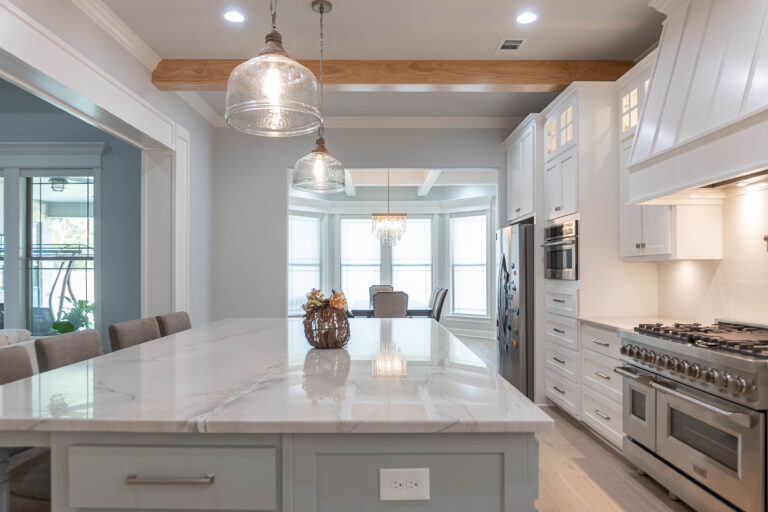 Esplanade kitchen to dining brown natural stain wood beam ceiling white marble counter top island shaker style cabinets with window light top