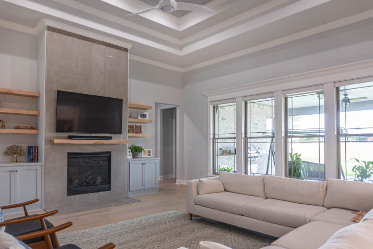 Esplanade living room white trim bank windows tan wood floors natural wood finish stain floating shelves grey tile floor to ceiling fireplace finish Beaumont home builder