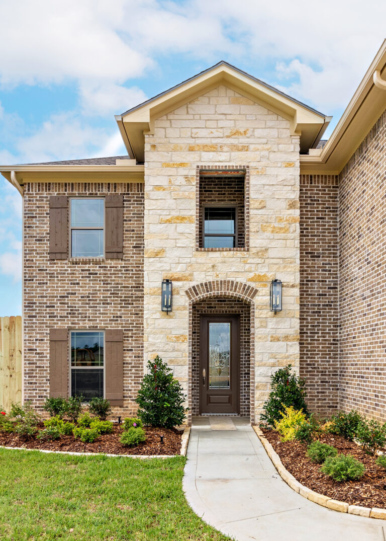 240 Riverstone Court two story home exterior entry with stone tower cased brick window opening above arch entry door brown tan brick